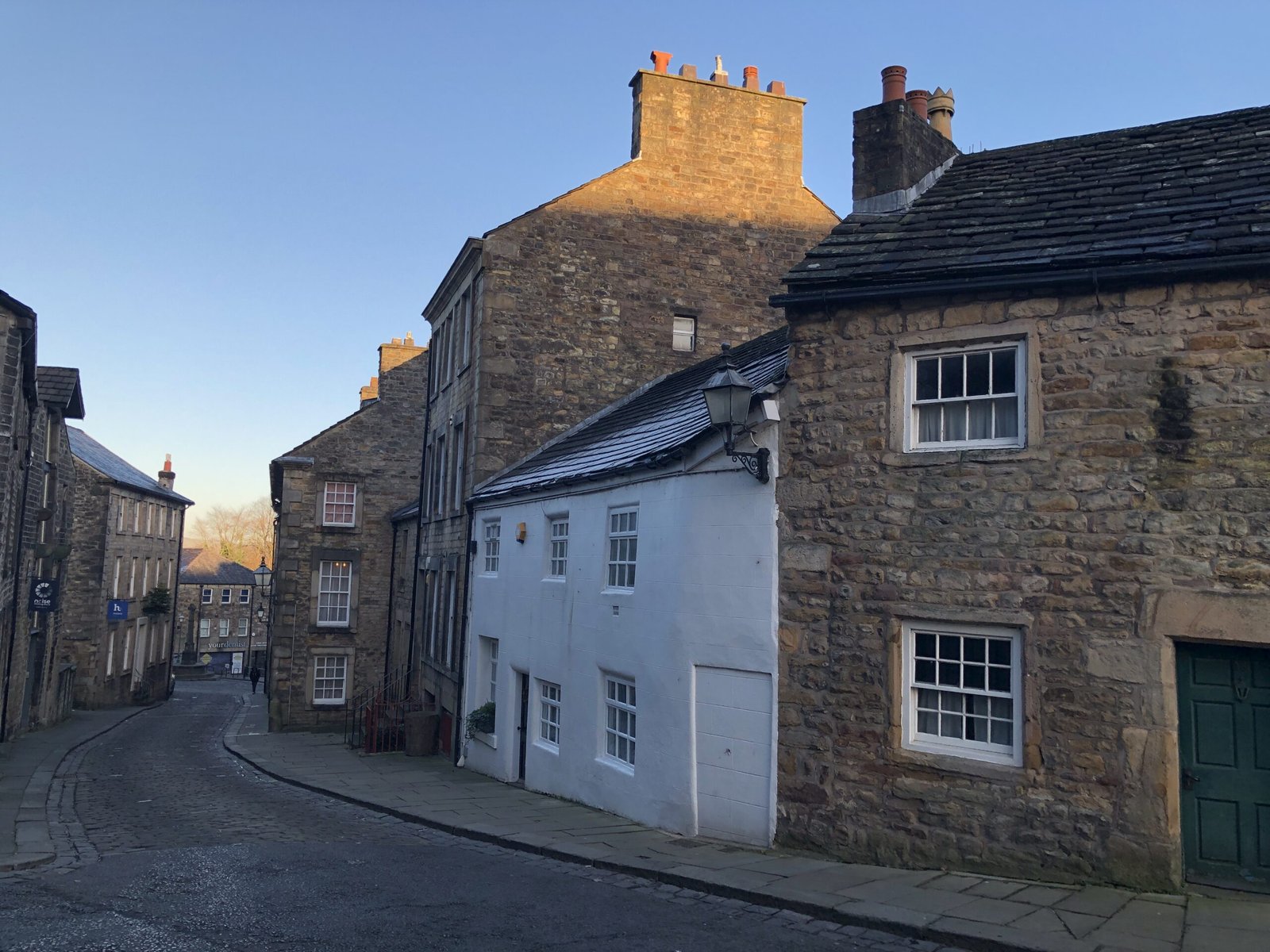 Historic cobbled street in Lancaster with stone cottages and Georgian buildings near the Cottage Museum at sunset.